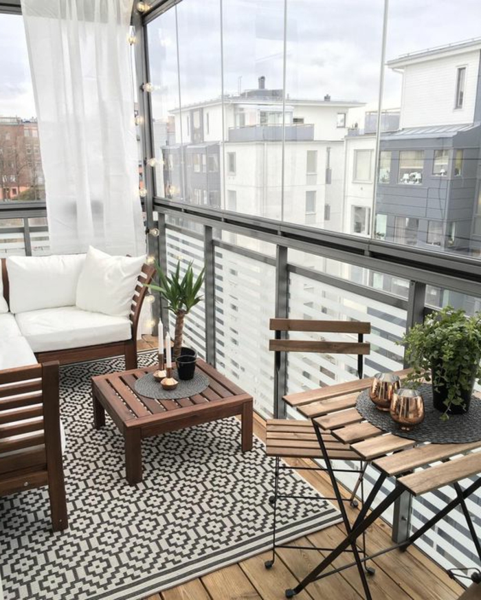 como decorar una terraza pequeña, balcón con suelo de madera y tapete, muebles de madera, cojines blancos, mesa con candelas y plantas