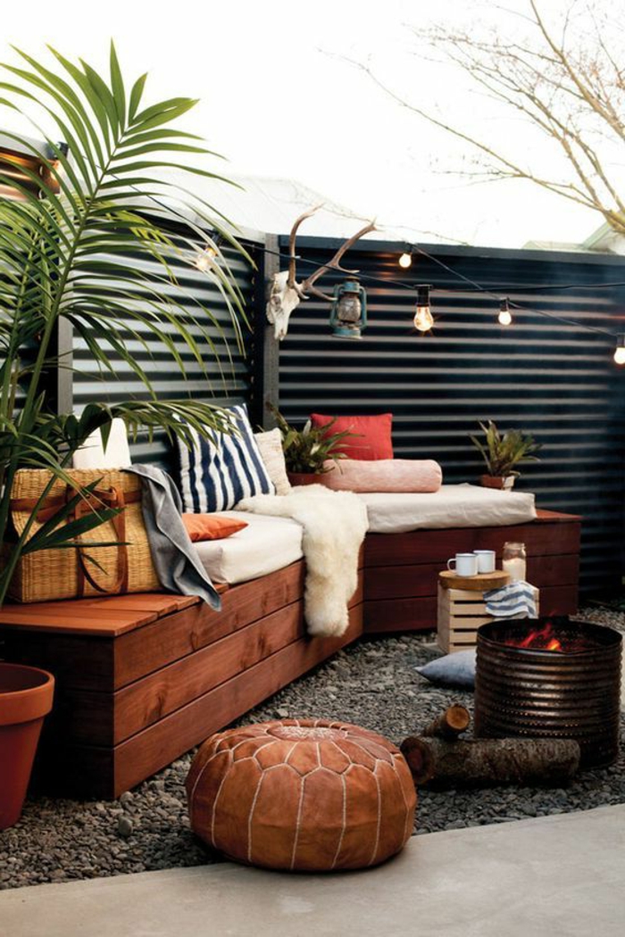 como decorar una terraza pequeña, terraza con suelo de gravilla, banca con cojines y cobija, fuego artificial