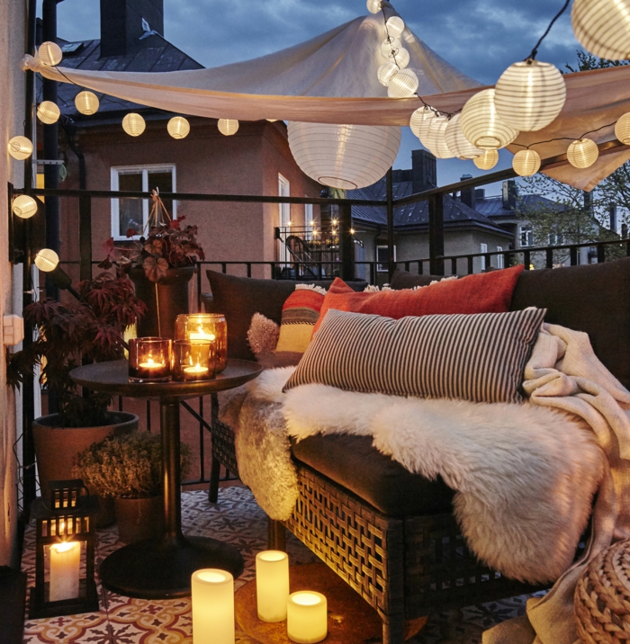 decoracion de terrazas, balcón pequeño con sofá de rattan, mesa con candelas, cojines y globos de luz