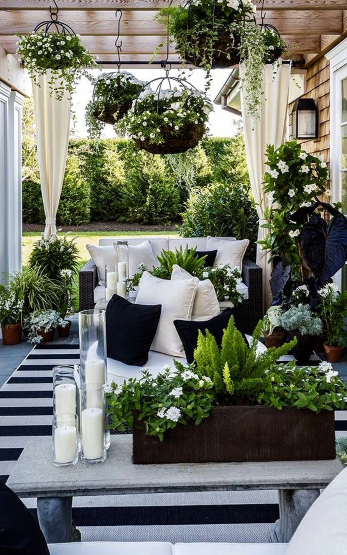decoracion de terrazas, terraza en blanco y negro, sofá con cojines, mesa con candelas y flores, macetas colgantes