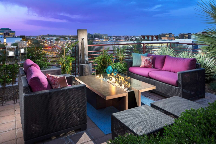 decoracion de terrazas-terraza con mesa de madera decorada con fuego artificial, sofás de rattan, cojines lila