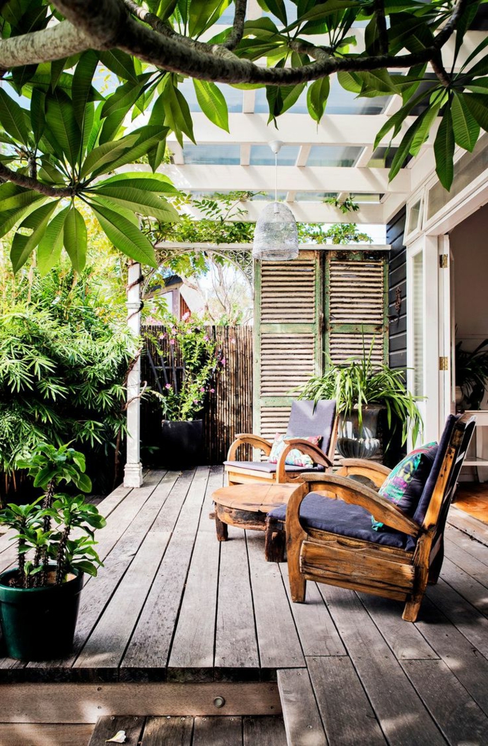 decoracion jardin, terraza con tarima, dos sillones de madera con cojines, mesa redonda, biombo y plantas verdes