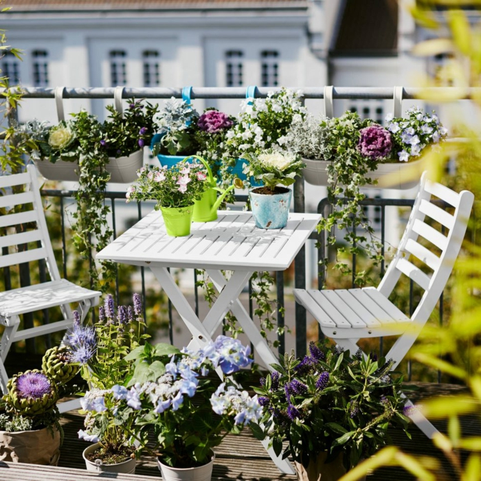 terrazas pequeñas, balcón lleno de flores, mesa y sillas de madera blanca