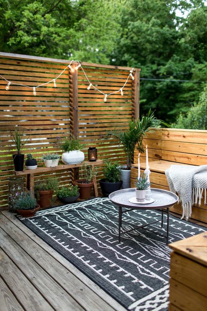 terrazas pequeñas, terraza de madera, mesa redonda de metal con portavelas, tapete blanco y negropç, banca y plantas