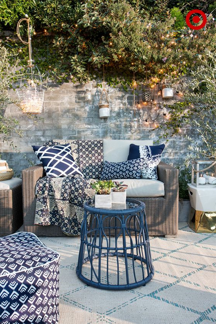 terrazas pequeñas, terraza en marrón y azul, sofá de rattan, mesita, pared de ladrillo con portavelas colgantes