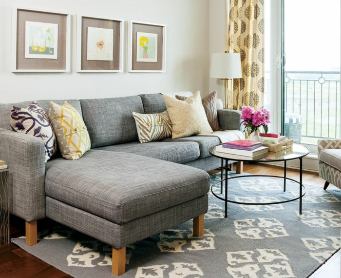 salones pequeños, salón con sofá gris en forma de L, tres cuadros, ventanal y mesa redonda de vidrio con flores