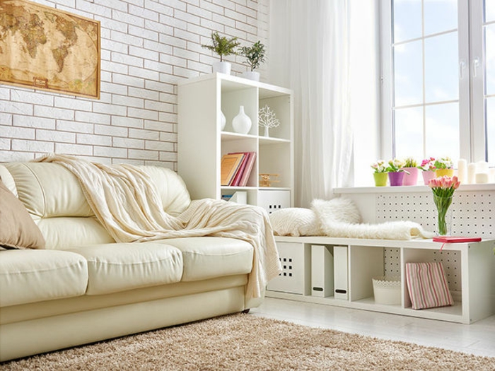 sslon, espacio pequeño con ventana grande, sofá de piel beige, pared de ladrillo blanco con mapa del mundo, estantería blanca con flores
