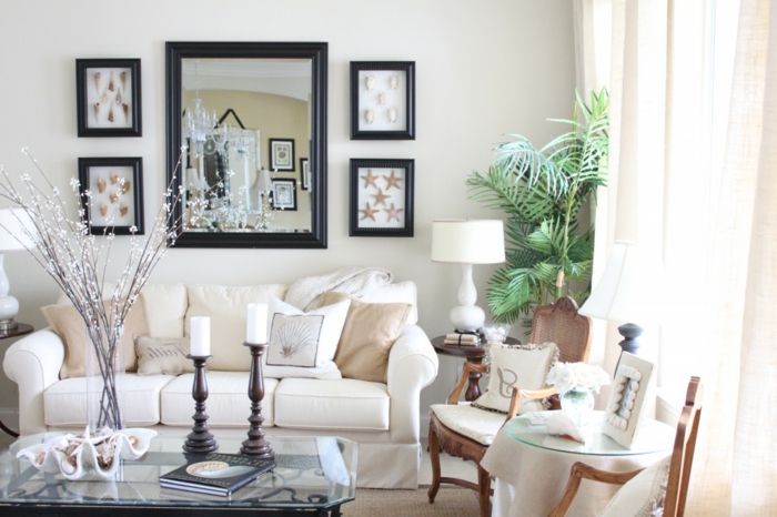salones modernos, salón con espejo grande, sofá blanca con cojines beige, mesa de vidrio con candelas y flores, dos sillas, planta verde