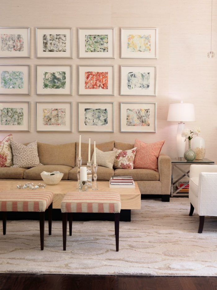 decoracion de interiores salones, salón con mesa de madera y portavelas, sofá beige con cojines rosados, muchos cuadros con motivos florales