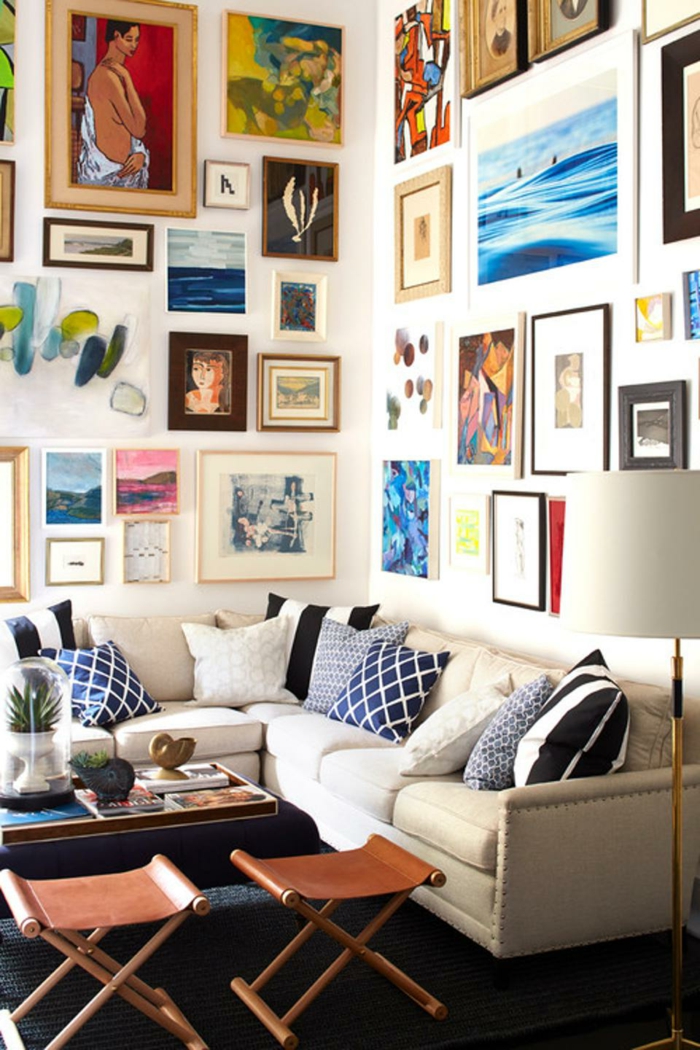 salon, paredes llenas de cuadros, sofá en forma L con cojines en tonos azules, dos sillas plegables y mesa