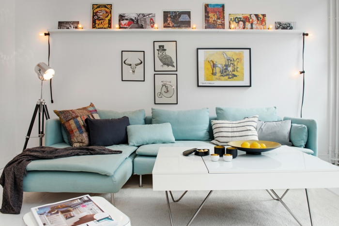 salon, sofá azul en forma de L y cojines, mesa cuadrada blanca de plástico, bombillas encentdidas y cuadros con animales y bicicleta retro