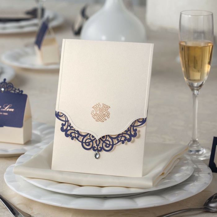 invitaciones creativas, invitación elegante en dorado y azul sobre mesa con vaso de champaña