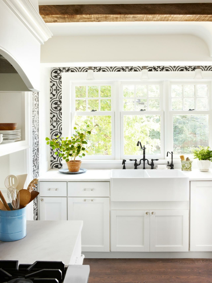 cocinas modernas blancas, cocina pequeña, fregadero blanco bajo ventanas, decoración con figuras negras, techo con vigas de madea