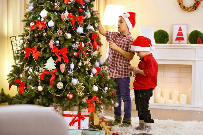 arbol de navidad decorado con cintas en moño rojas, pequeñas bolas y ornamentos en diferentes colores, corona de navidad en la pared