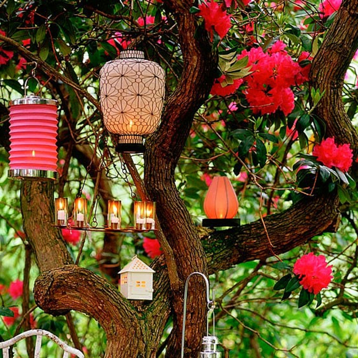 como hacer un jardín, lámparas bonitas de diseño y tamaño diferente, colgadas en el árbol de flores rojas