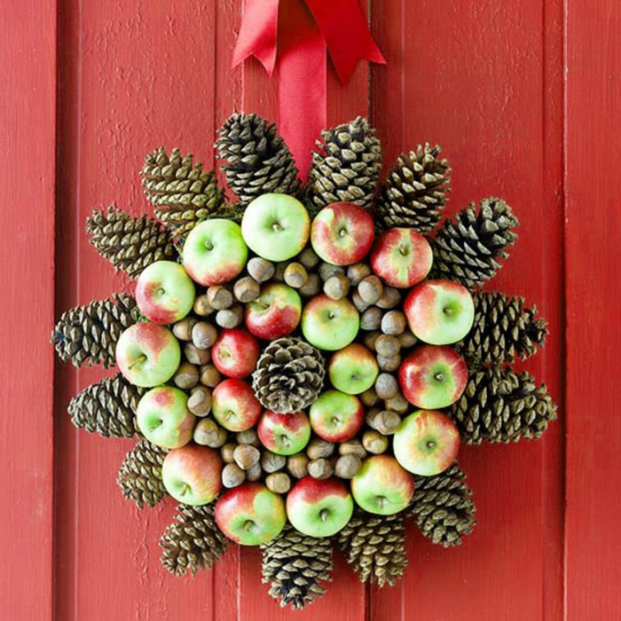 manualidades navidad, corona navideña natural de manzanas y piñas de pino, puerta de madera roja