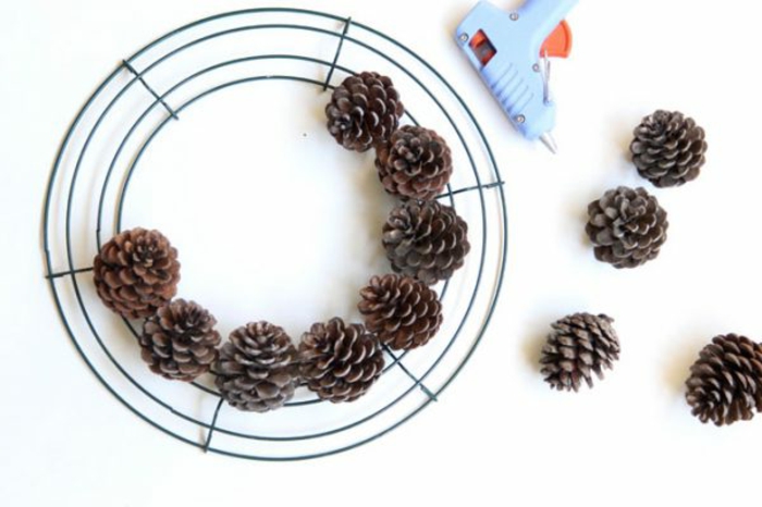manualidades navidad, cuerda circular de metal, piñas naturales, pistola encoladora, tutorial para hacer corona navideña en casa