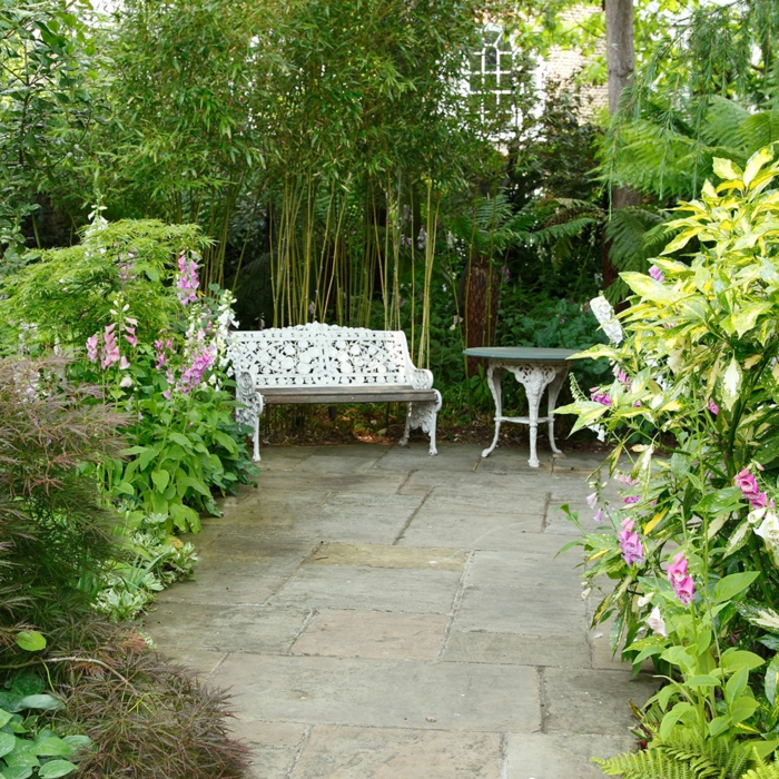 decoracion patios, bonito banco de madera, ornamentación que imita encaje, mesa redonda, arbustos grandes