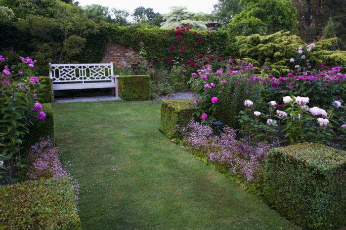 decoracion patios, césped rapada con arbustos de diseño, grande jardín con banco de madera blanco y muchas rosas