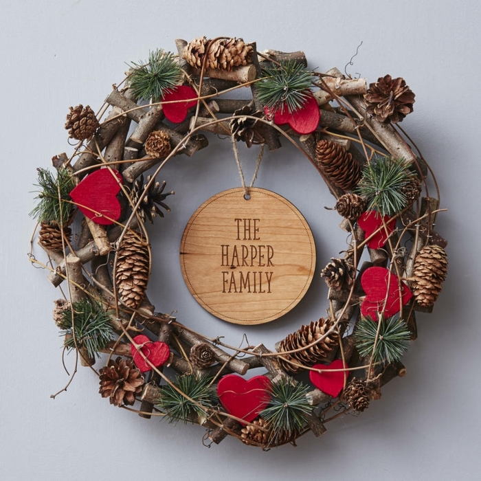 decoracion navideña casera, corona navideña natural de ramas, piñas y pino, corazones rojos, nombre de familia