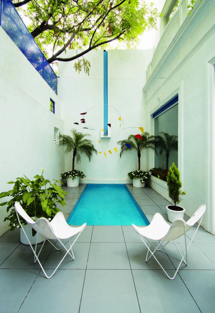 piscinas de obra, patio interno, piscina estrecha larga, sillas blancas, suelo de baldosas, plantas verdes en macetas