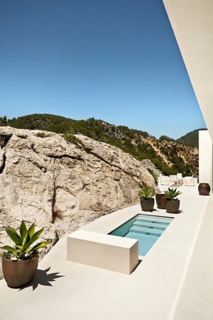 piscina desmontable, casa de campo moderna, paisaje con rocas, patio blanco con macetas, piscina pequeña con escalera integrada