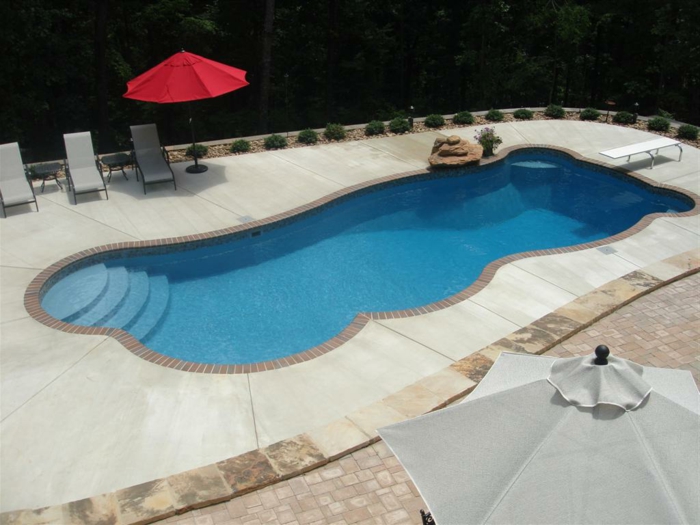 piscina desmontable, patio con suelo de baldosas, sombrilla roja y tres tumbonas, piscina con curvas y escalera integrada