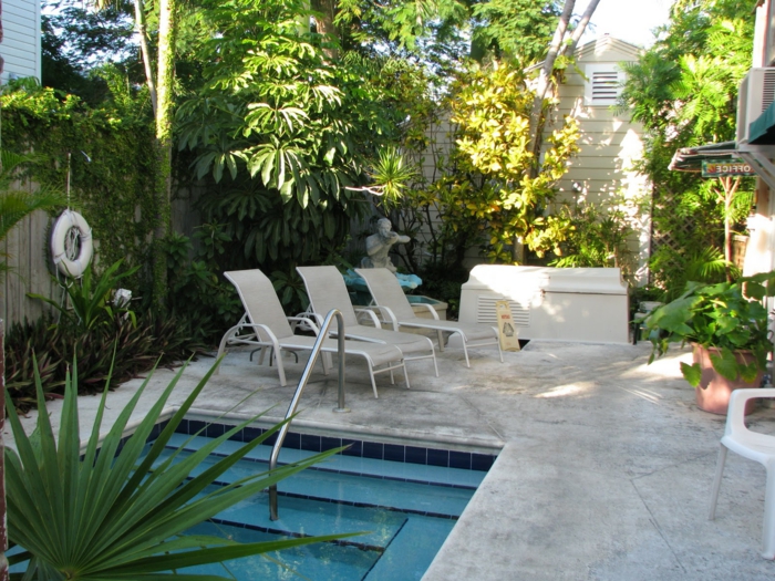 piscinas prefabricadas, patio con piscina pequeña con escalera integrada, estatua de hombre, tres tumbonas, plantas verdes