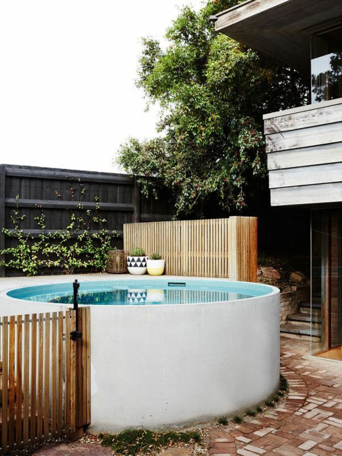 piscinas prefabricadas, patio con piscina de obra redonda blanca, valla de madera, balcon y árbol