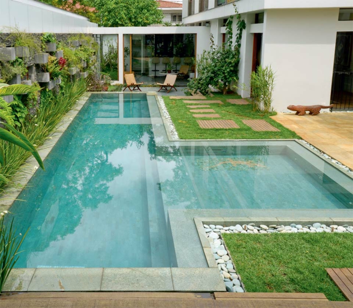 piscinas prefabricadas, patio con césped y piscina de obra en forma T, dos sillas, edificio blanco