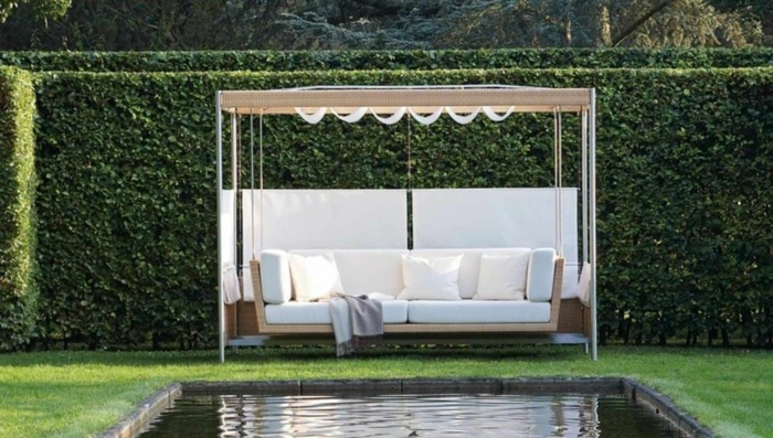 jardines modernos, tendencias 2018, bonito seto vivo alto y lago grande, pérgola moderna con sofá tipo cuña en beige y blanco