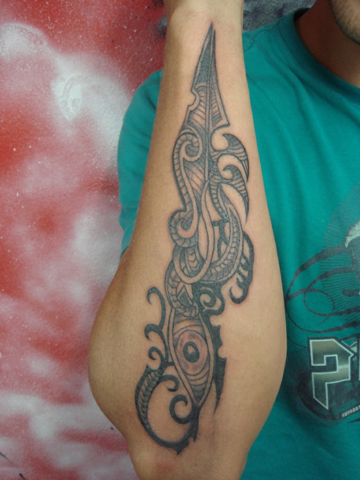 tatuaje maori, hombre con camiseta verde, tatuaje en antebrazo con ojo y símbolos polinesios