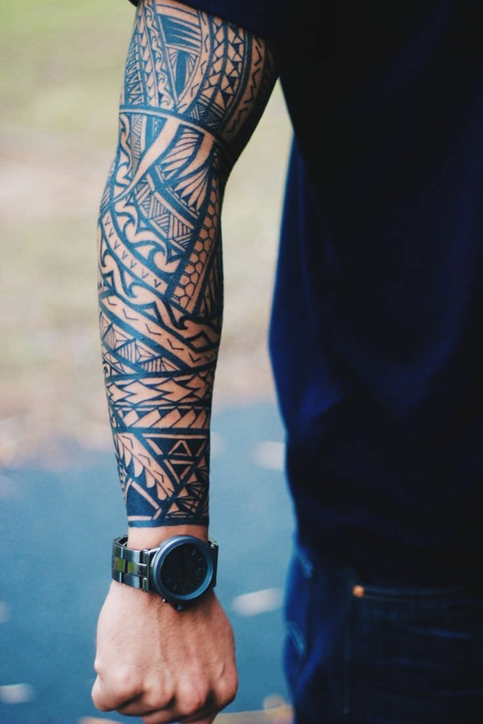 tatuajes brazo, hombre con camiseta negra y reloj, brazo entero tatuado, tatuaje polinesio con punta de lanza, dientes de tiburón