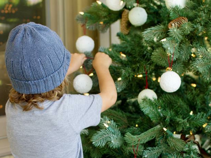 adornos navideños caseros, pequeño niño adornando el árbol navideño, bolas de poliestireno decoradas en blanco 