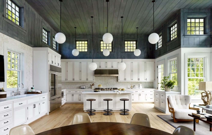 cocinas americanas, espacioso ejemplo en blanco y negro, techo de vigas de madera, suelo de parquet en color claro, muebles en blanco, barra con tres sillas de metal