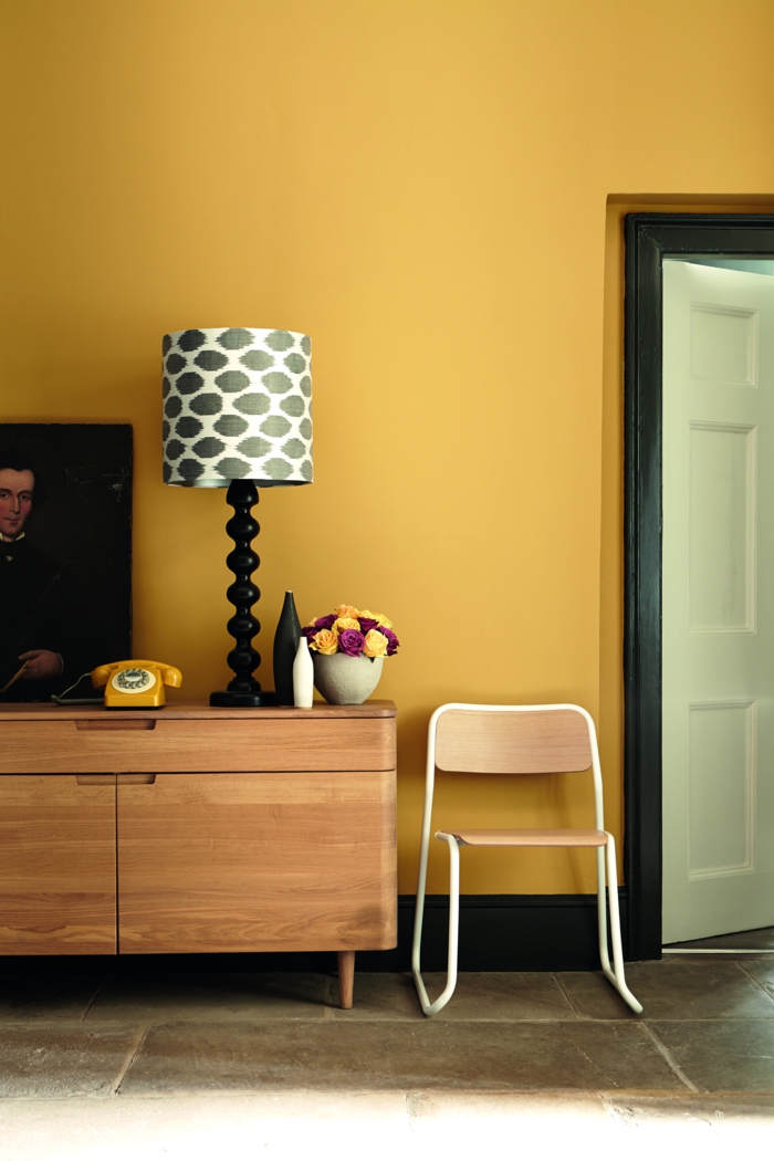 colores calidos, pared en color amarillo mostaza con detalles en negro, armario de madera, teléfono retro, cuadro clásico y decoración de flores
