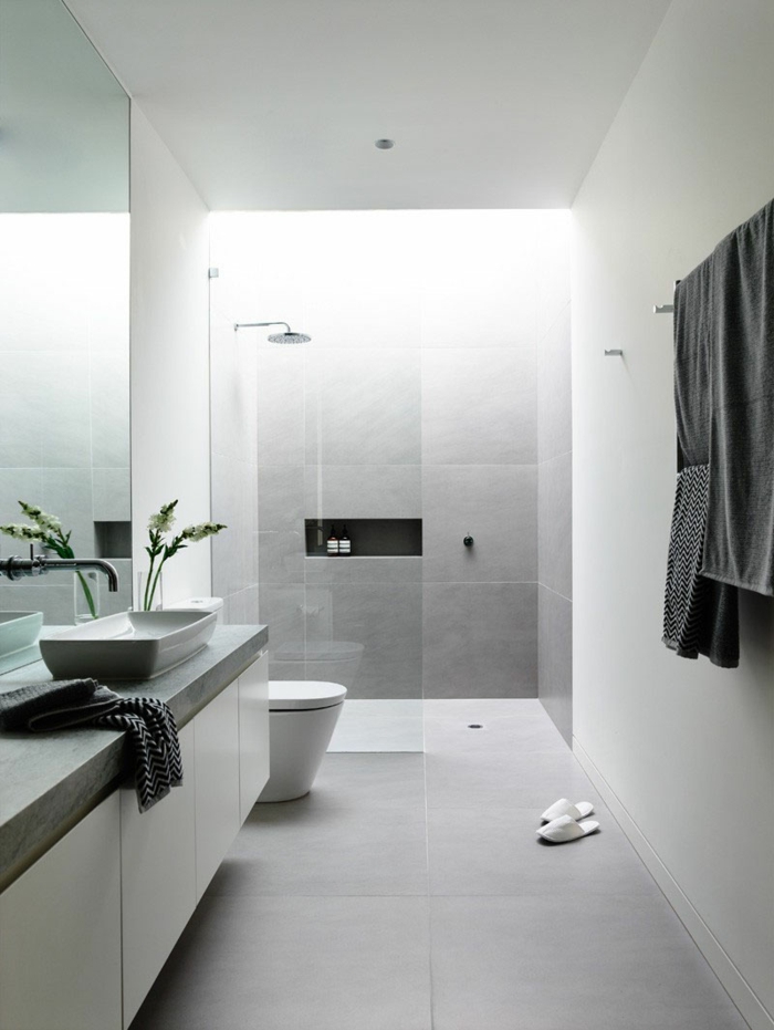 cuartos de baño con ducha, baño llargo y estrecho en color gris, ducha de obra con nicho en la pared, mampara de vidrio