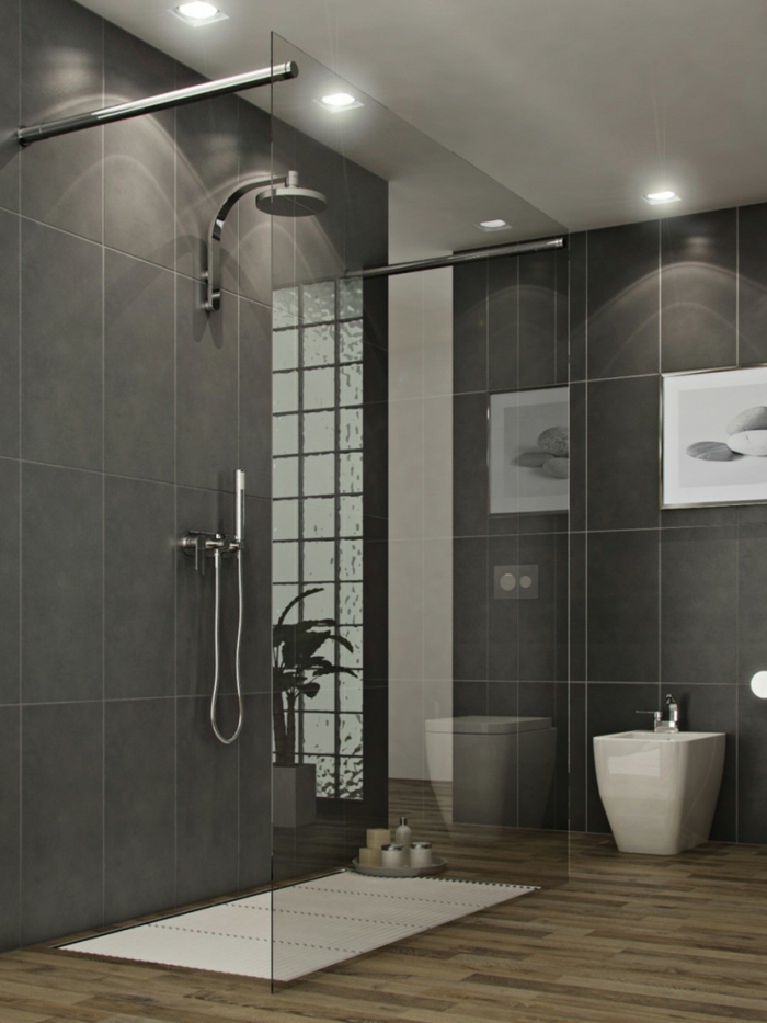 cuartos de baño con ducha, baño con suelo de madera y paredes con baldosas gris, cuadro con piedras, ducha de obra con rejilla blanca y mampara de vidrio