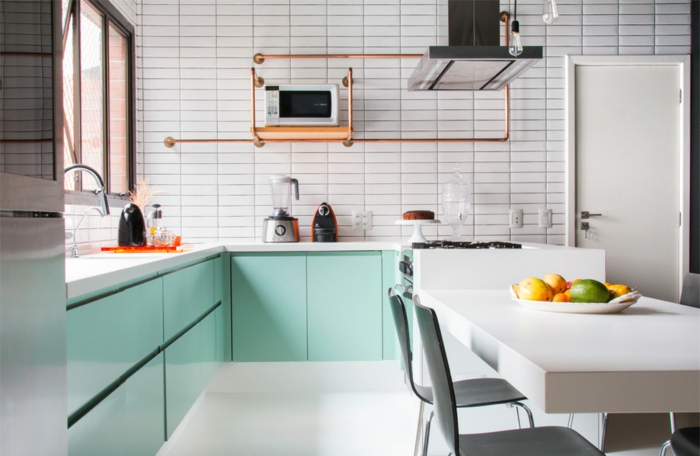 salon cocina en tonos claros, armarios en color verde menta, paredes con azulejos en blanco, mesa blanca, detalles en bronce