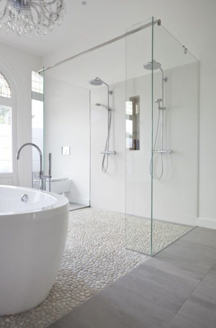duchas modernas, baño grande con ventanales, suelo con baldosas y piedrirtas, bañera. ducha doble con mampara de vidrio, lámpara de araña