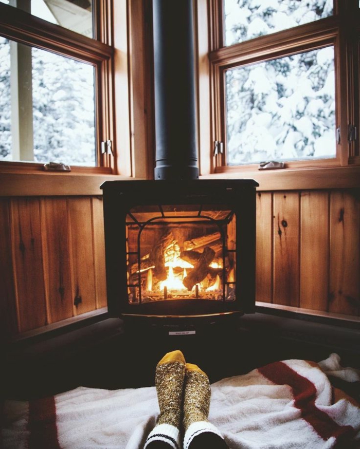 estufa leña, cama acogedor al lado de la estufa de leña, casa rural con paredes con vigas de madera, ventanas con vista invernal
