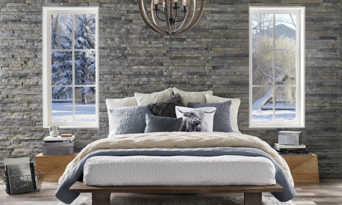 revestimiento paredes, dormitorio con cama doble y lámpara de araña, dos ventanas paralelas con vista a un jardín durante el invierno, pared de piedra decorativa gris