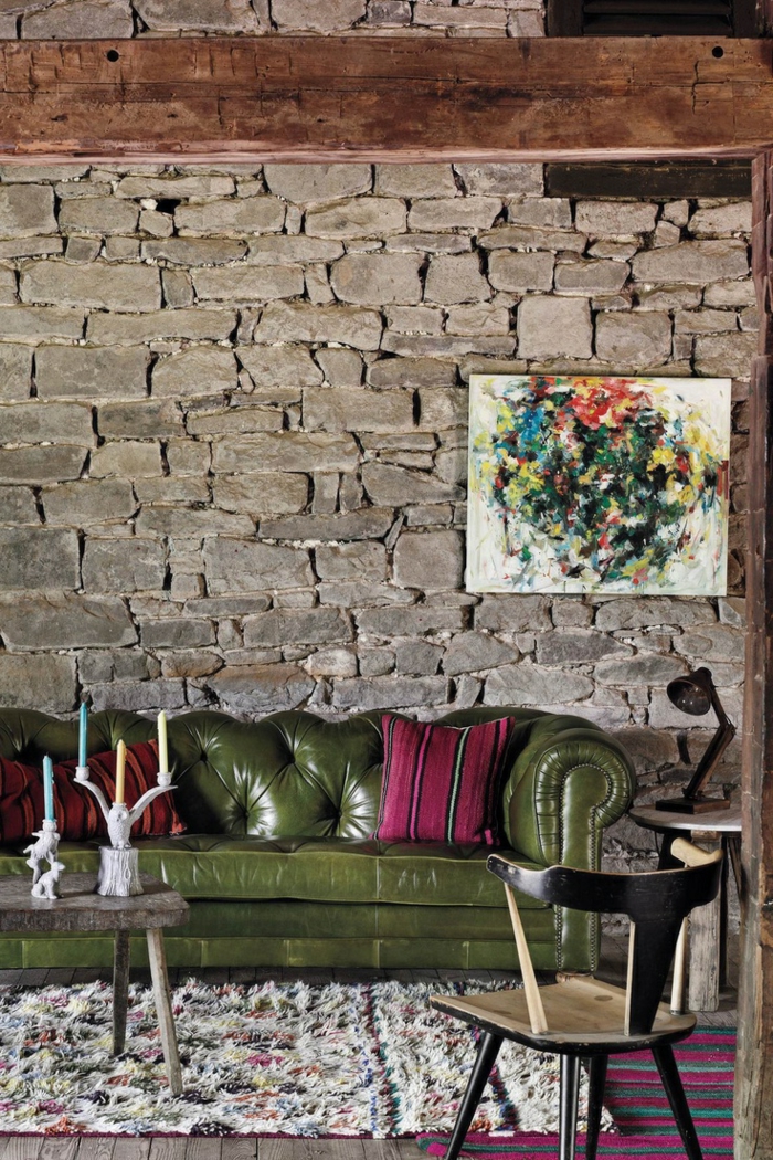 pared de piedra, salón moderno con sofá tapizada de piel, cuadro abstracto, mesa con portavelas, pared de piedra rustica