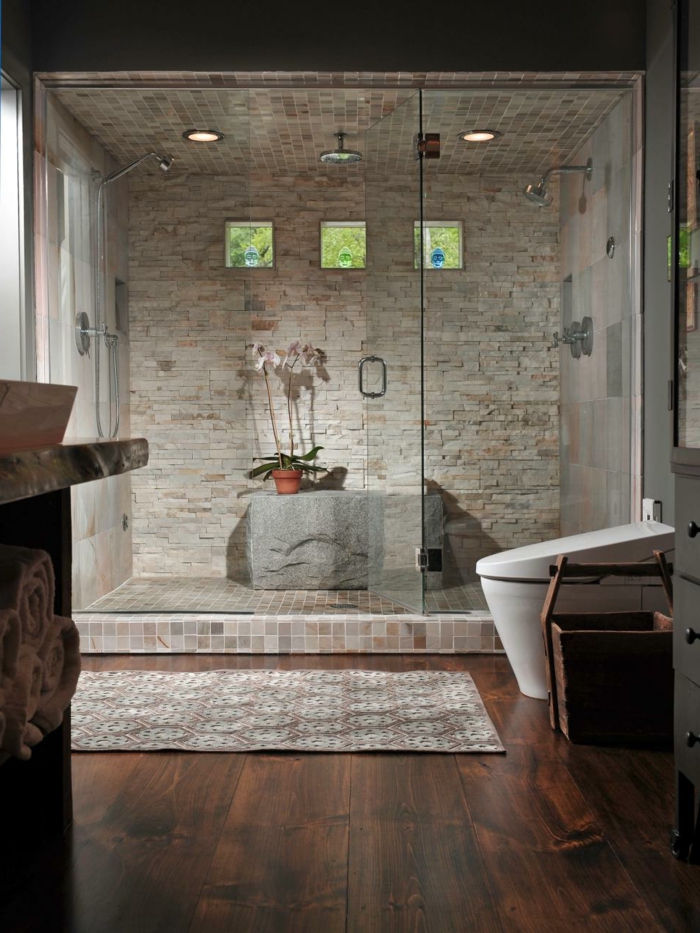 duchas modernas, ducha de obra separada con mampara de vidrio, baño con suelo de tarima, pared de piedra, tres pequeñas ventanas