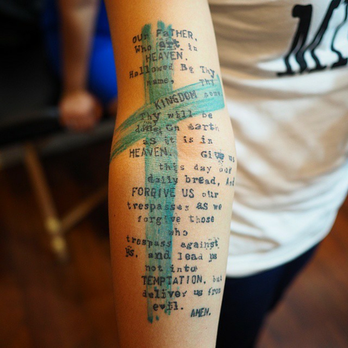 tipos de tatuajes, mujer con tatuaje de antebrazo, texto del rozo padre nuestro en fuente de máquina de escribir, cruz en zul