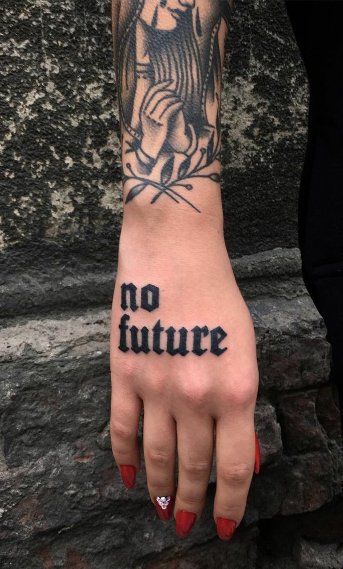 tatuajes letras, con tatuaje de antebrazo y mano, tatuaje con frase de letras en bloque negras, uñas con esmalte rojo