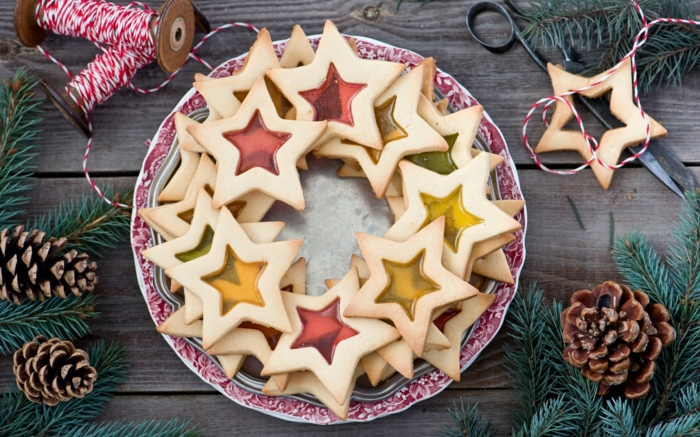 estrella navidad, galletas estrellas con gelatina en rojo y amarillo, decoración de piñas y ramos de pino, carretes de hilo 