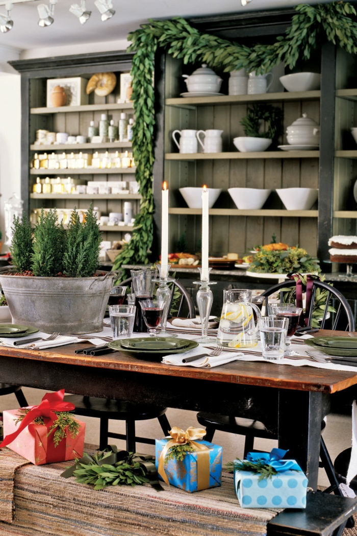 centro de mesa, comedor en estilo rústico, decoración en verde, centro de mesa con pinos enanos en un macetero de metal, regalos puestos en el banco de madera