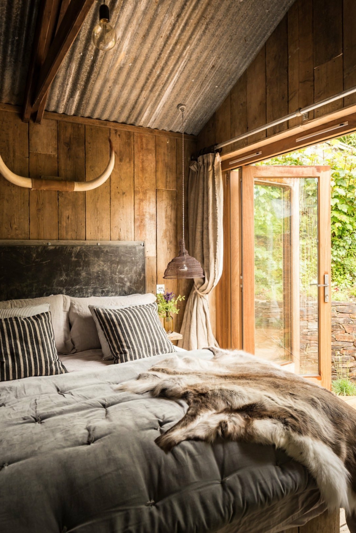 casa de madera, precioso dormitorio en estilo rústico, cama de madera con cabecero, cobijas de piel 