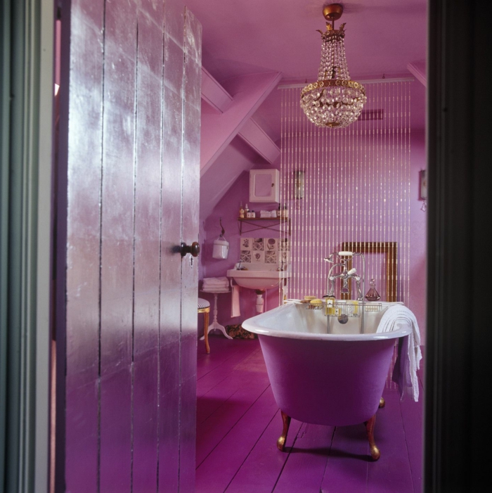 muebles de baño, idea extravagante en color lila saturado, puerta y suelo de madera, lámpara de araña con ornamentos de cristal, bañera patas garra